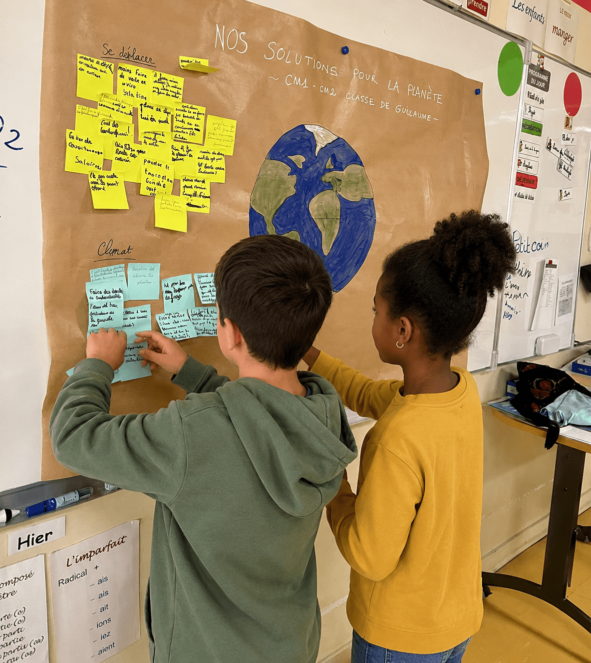 Deux enfants collent des post-it sur un panneau de classe